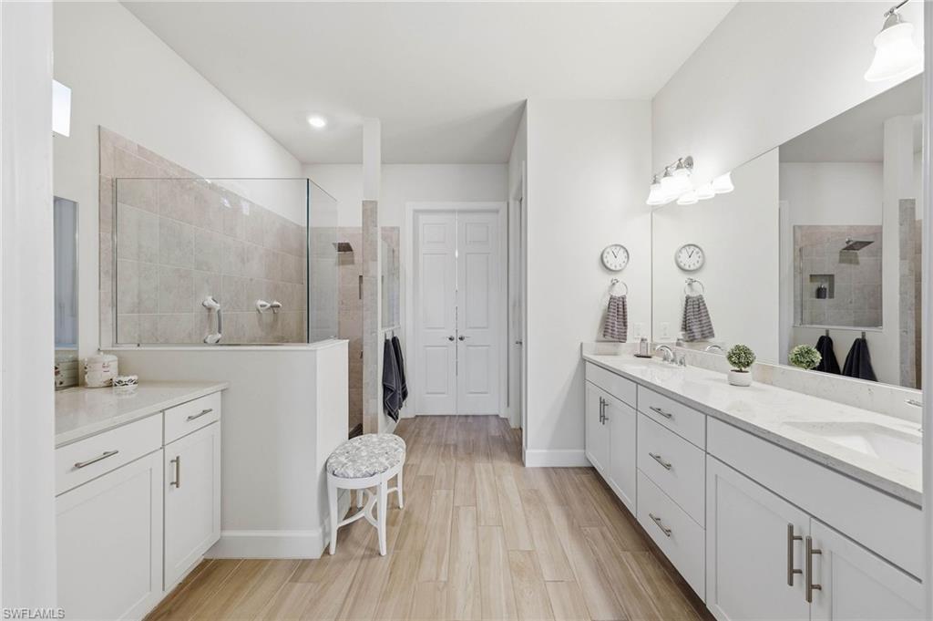 Spacious primary bathroom featuring a dual vanity with white cabinetry and light countertops, and an expansive tiled shower with a glass enclosure, large walk in closet