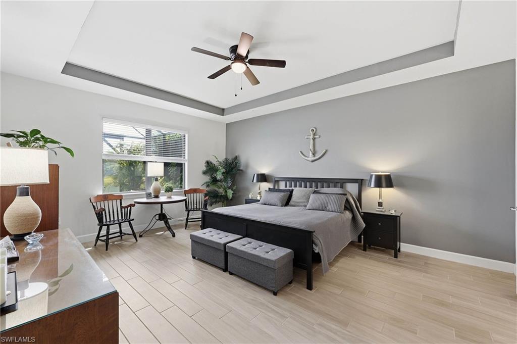 Spacious primary bedroom featuring light tile  flooring, tray ceiling with a ceiling fan and sitting area