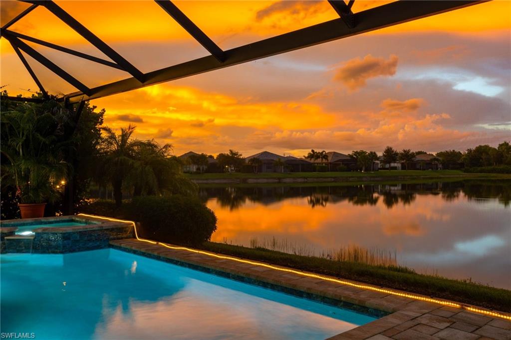 Screened lanai featuring a swimming pool, integrated spa, and illuminated patio pavers bordering a lake