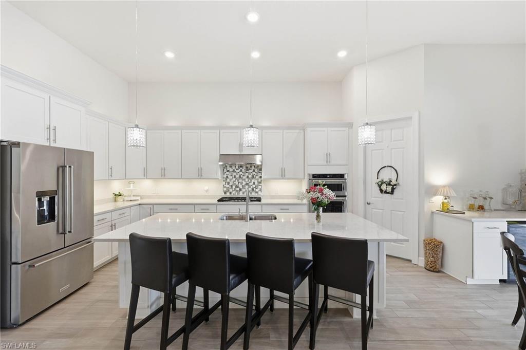 Spacious kitchen with a large central island, under cabinet lighting, walk in pantry, stainless steel appliances, white cabinetry, additional bar area