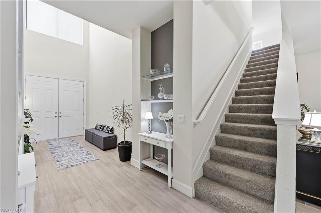 Two-story foyer featuring double entry doors, natural light , wood tile flooring, a carpeted staircase, and built-in shelving with glass accents