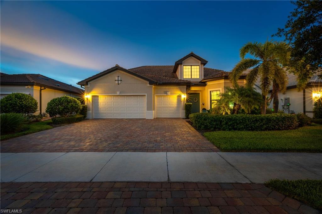 Front exterior featuring a 3 car extended garage, mature landscaping, and an illuminated entryway