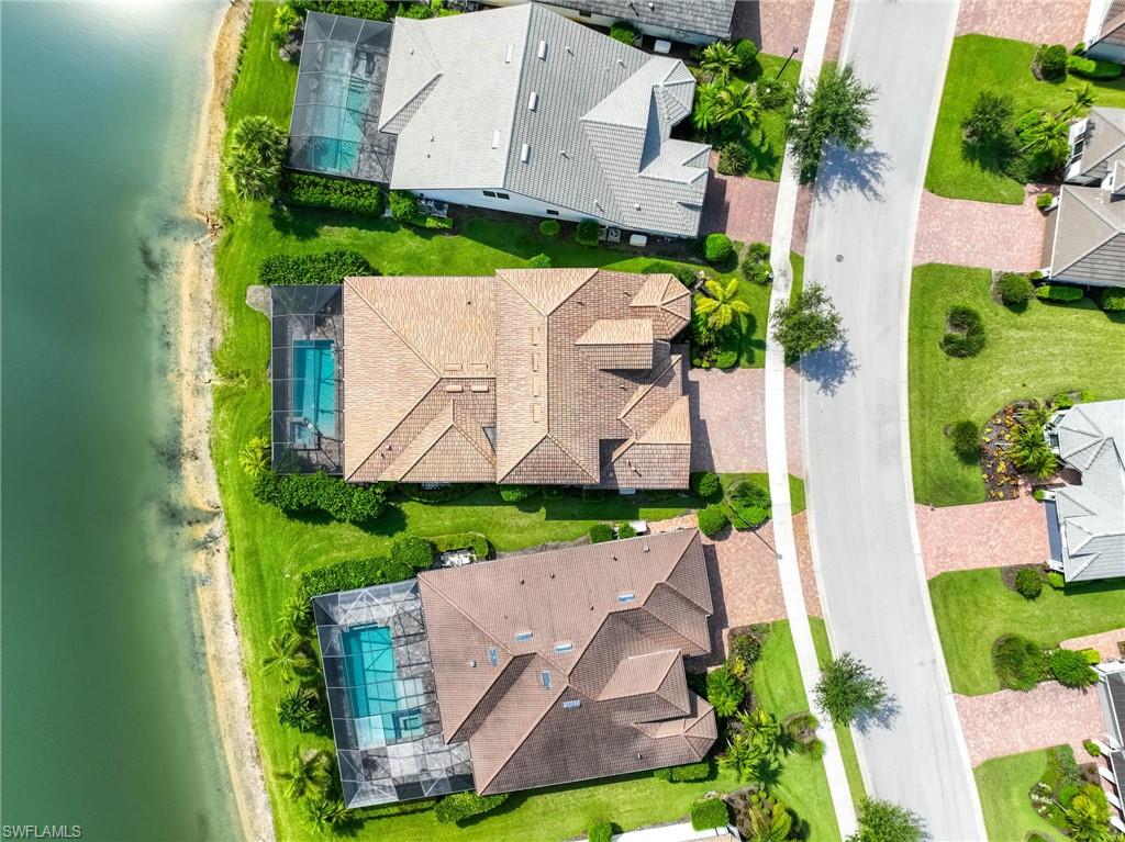Aerial view showcasing a property with a distinct roofline, a screened pool enclosure, and lush surrounding landscaping