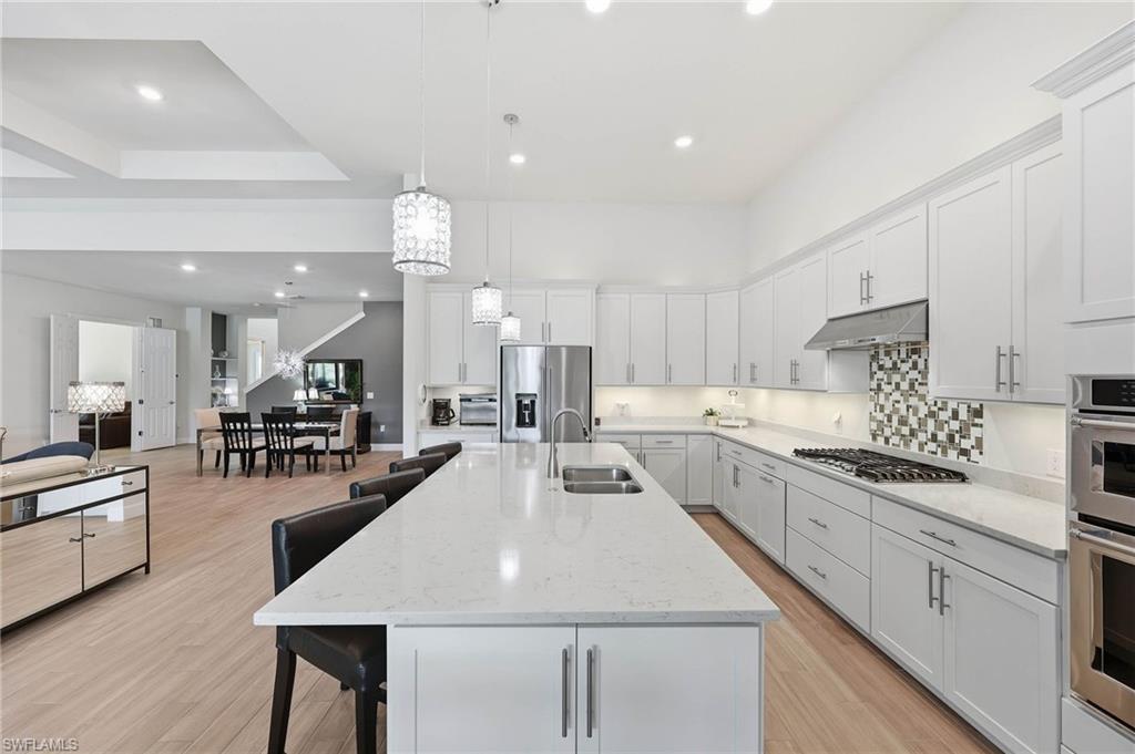 Spacious kitchen featuring an extended center island with integrated dual sink, white cabinetry with plenty of storage, and neutral tile backsplash
