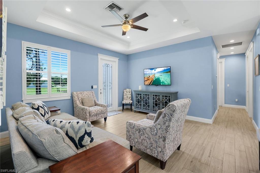 Spacious living area featuring light wood-finish flooring, a tray ceiling with recessed lighting, and a ceiling fan
