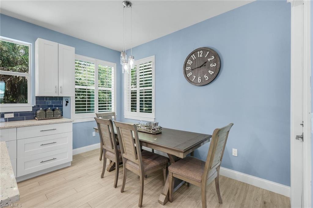 Kitchen and dining area featuring light wood-finish flooring, white cabinetry, a blue subway tile backsplash, and a pendant light fixture