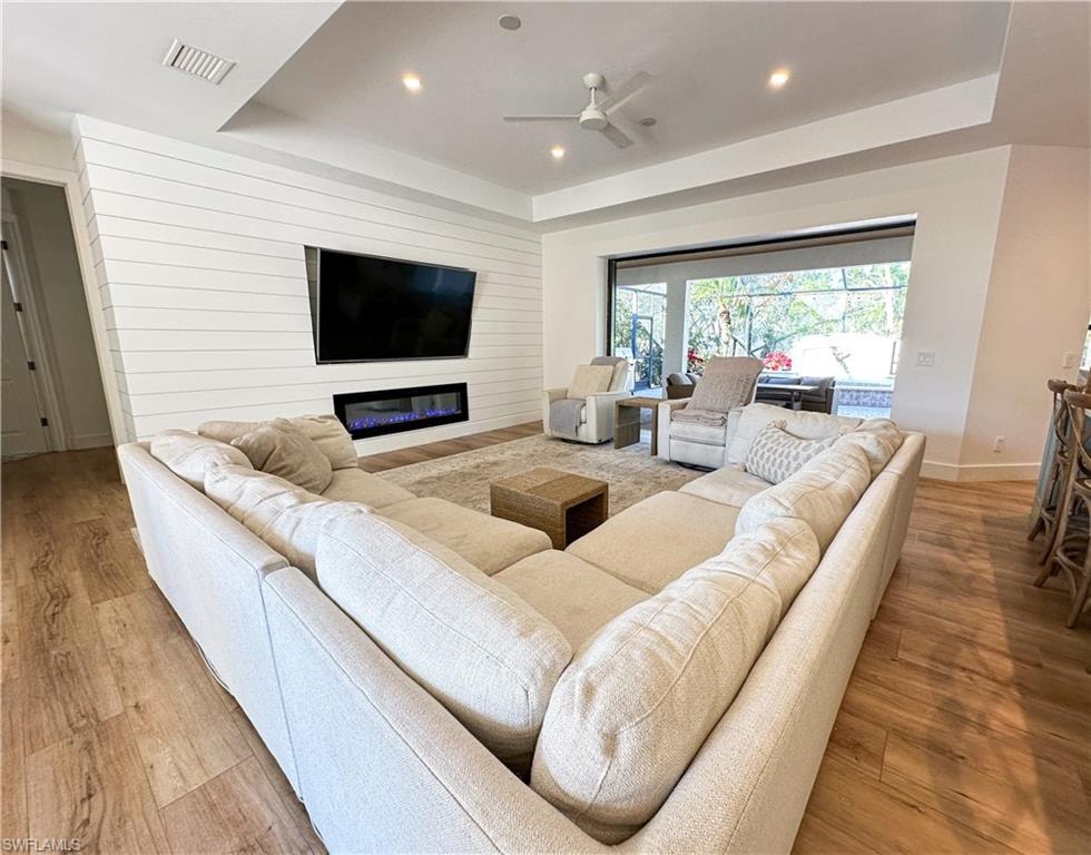 Living room featuring ceiling fan, a tray ceiling, and light hardwood / wood-style flooring