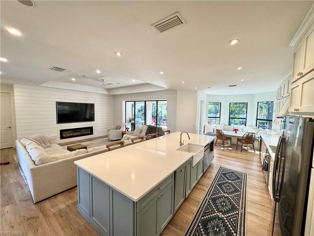 Kitchen featuring visible vents, open floor plan, a kitchen island with sink, light countertops, and a sink