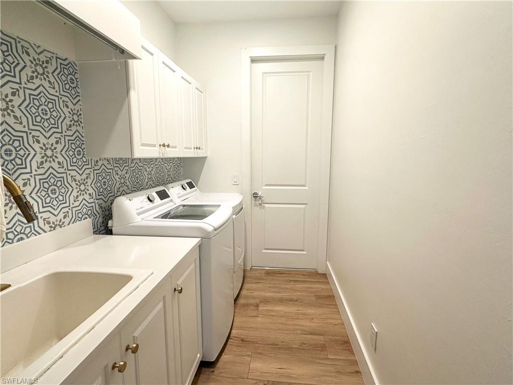 Washroom featuring cabinets, sink, washer and clothes dryer, and light hardwood / wood-style floors