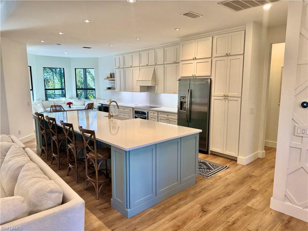 Kitchen with stainless steel appliances, a sink, open floor plan, light countertops, and an island with sink