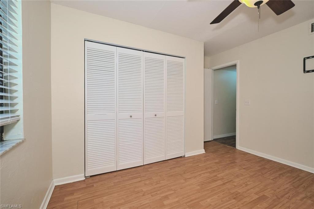 Room featuring wood-finish flooring, louvered bi-fold closet doors, a ceiling fan, and a window with blinds