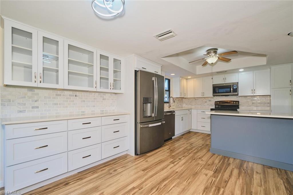 Spacious kitchen featuring wood-finish flooring, white cabinetry with glass-front uppers, a subway tile backsplash, and a central island with a contrasting base