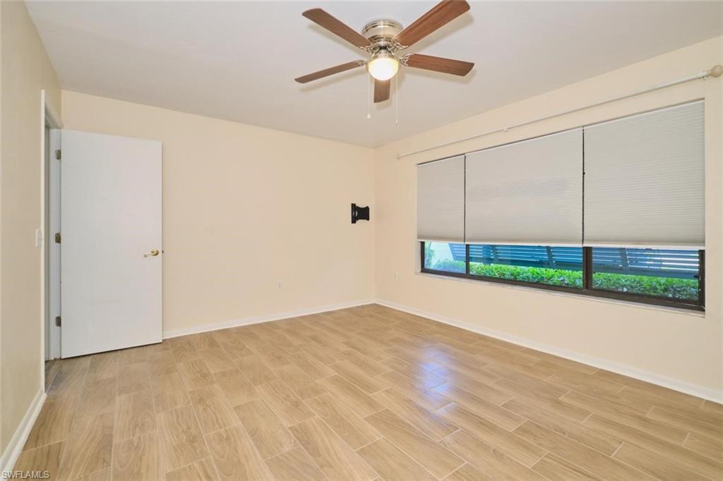 Spacious room featuring wood-finish flooring, a ceiling fan with integrated lighting, and a wide window with roller blinds
