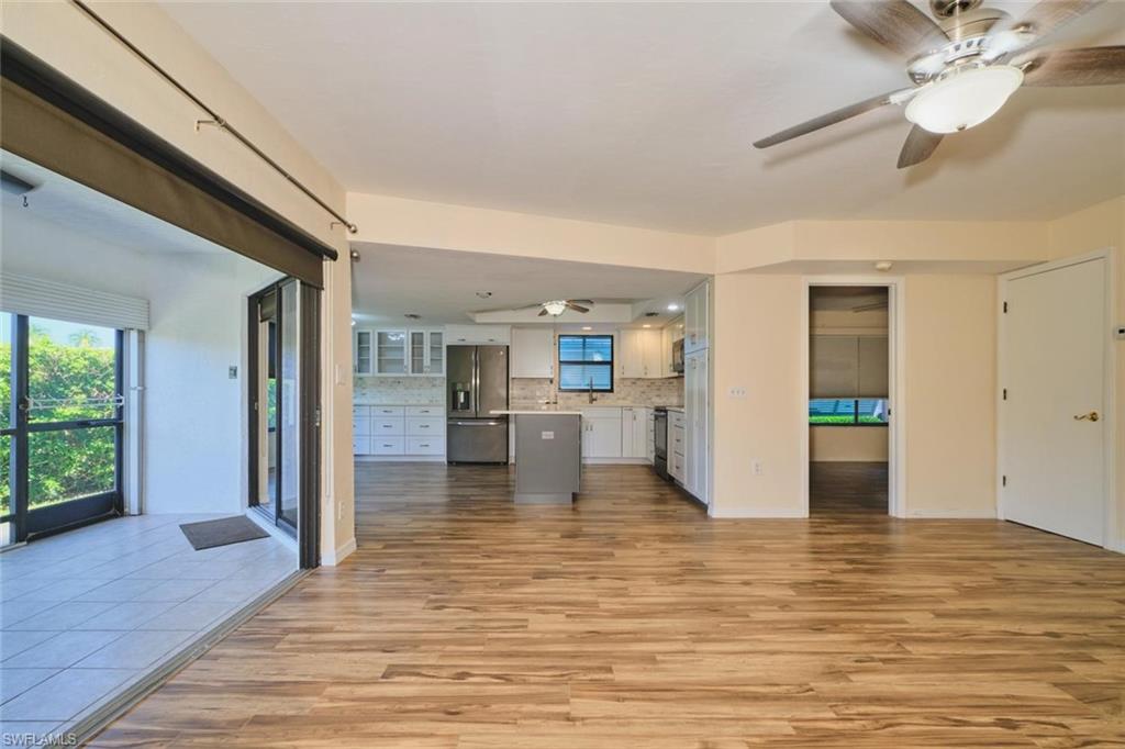 Open-concept interior featuring wood-finish flooring, a contemporary ceiling fan with integrated lighting, and a modern kitchen with stainless steel appliances, light cabinetry, and an island with a contrasting base
