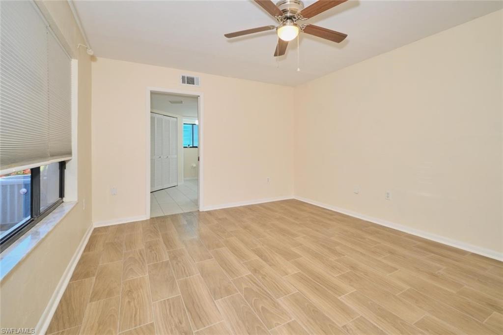 Spacious room featuring wood-finish tile flooring, neutral wall tones, and a ceiling fan with integrated lighting