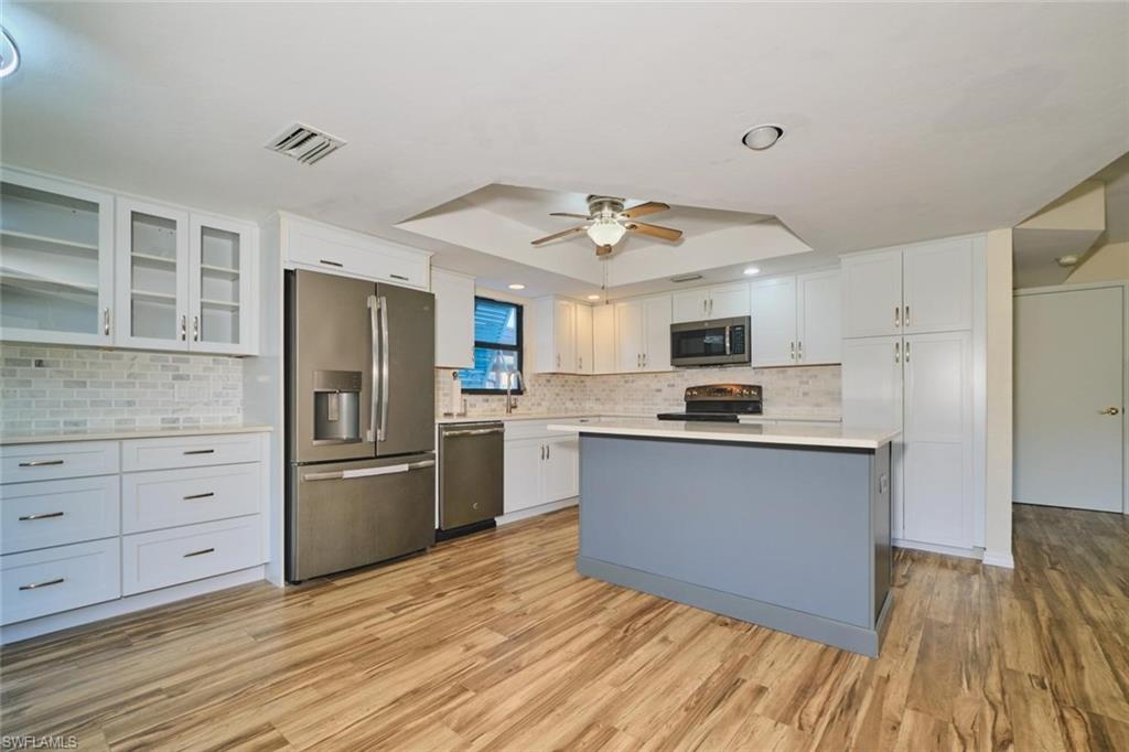 Kitchen featuring wood-finish flooring, white cabinetry with display uppers, and stainless-steel appliances