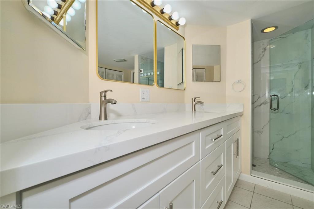 Double vanity with white cabinetry, integrated sinks, brushed nickel faucets, and a frameless glass shower enclosure featuring a white and gray tiled surround
