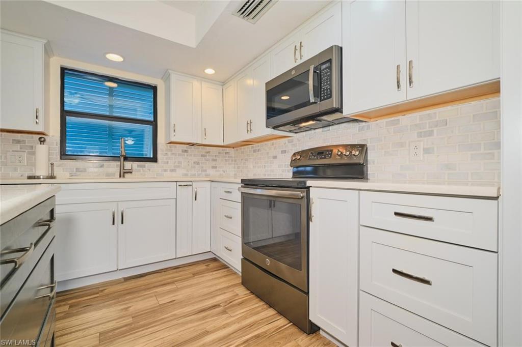 Modern kitchen featuring white shaker cabinetry, stainless steel appliances, a light-toned brick pattern backsplash, wood-finish flooring, and recessed lighting