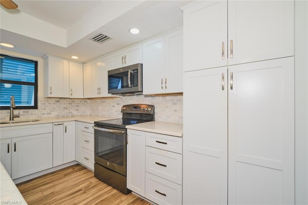 Modern kitchen featuring white shaker cabinetry, stainless steel appliances, light-toned countertops, a mosaic tile backsplash, and wood-finish flooring
