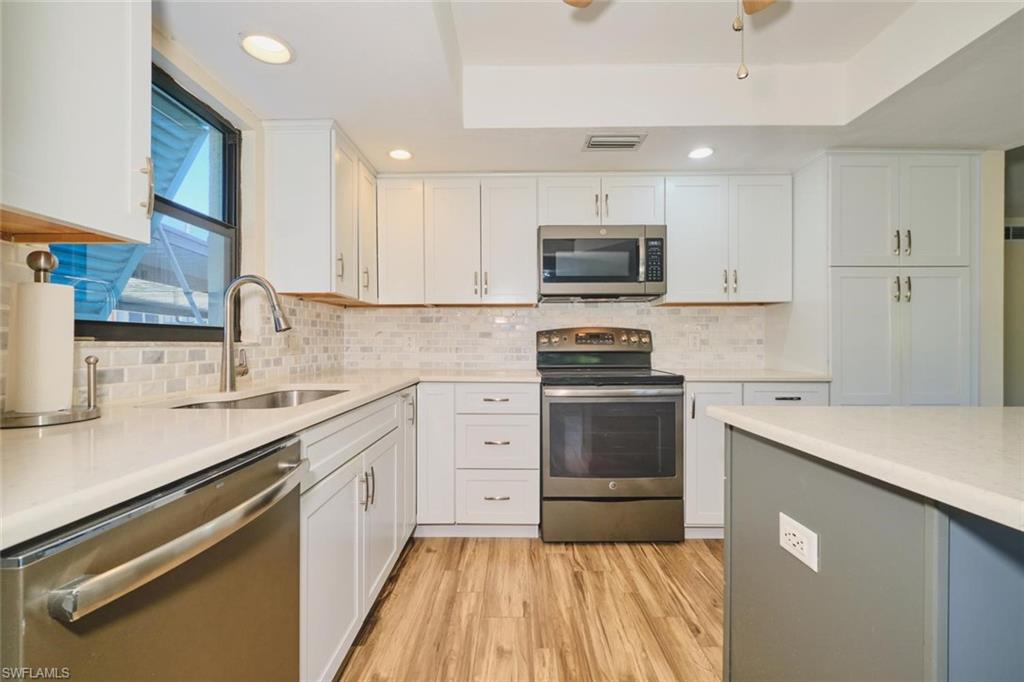 Modern kitchen featuring white shaker cabinetry, stainless steel appliances, light countertops, a mosaic tile backsplash, and wood-finish flooring