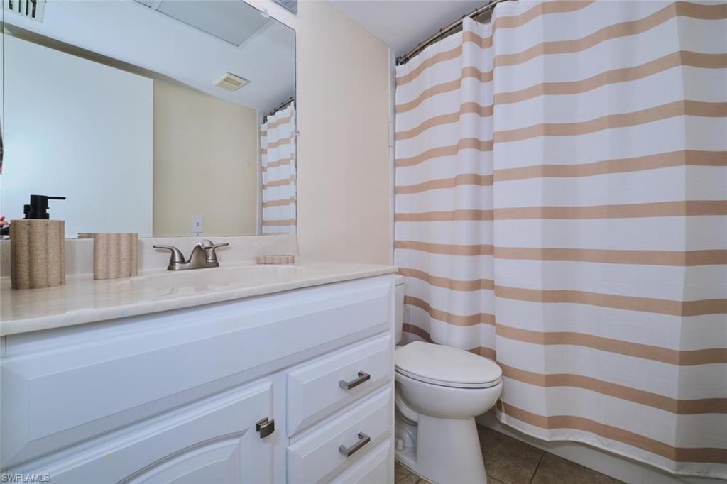 Bathroom featuring a vanity with a light-toned countertop, a rectangular mirror, a toilet, and a tiled shower area