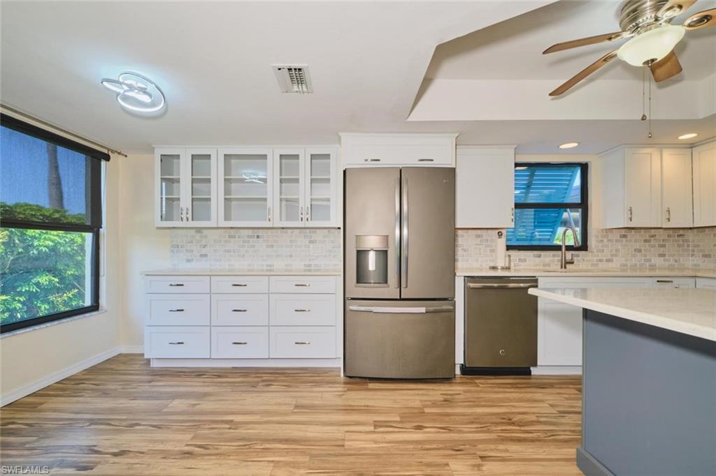 Updated kitchen featuring stainless steel appliances, white cabinetry with glass-front uppers, a full tile backsplash, and wood-finish flooring