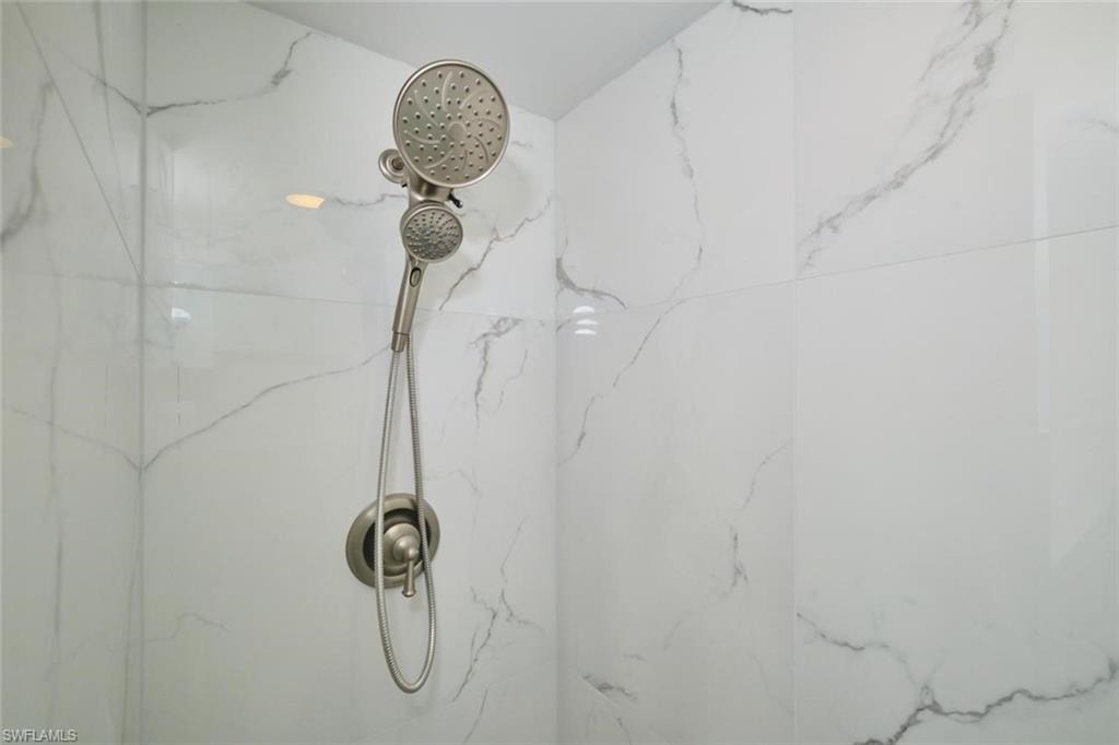 Shower enclosure featuring large format white tiled walls with gray veining, a brushed nickel showerhead, and a matching handheld shower sprayer