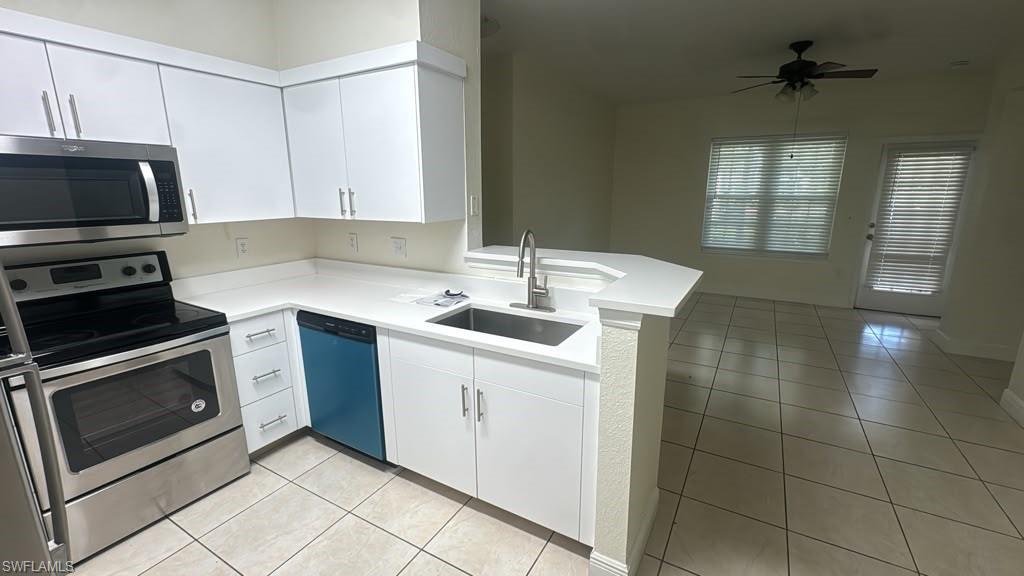 Kitchen featuring white cabinetry, stainless steel appliances, a corner sink with a gooseneck faucet, light-toned countertops, and tile flooring