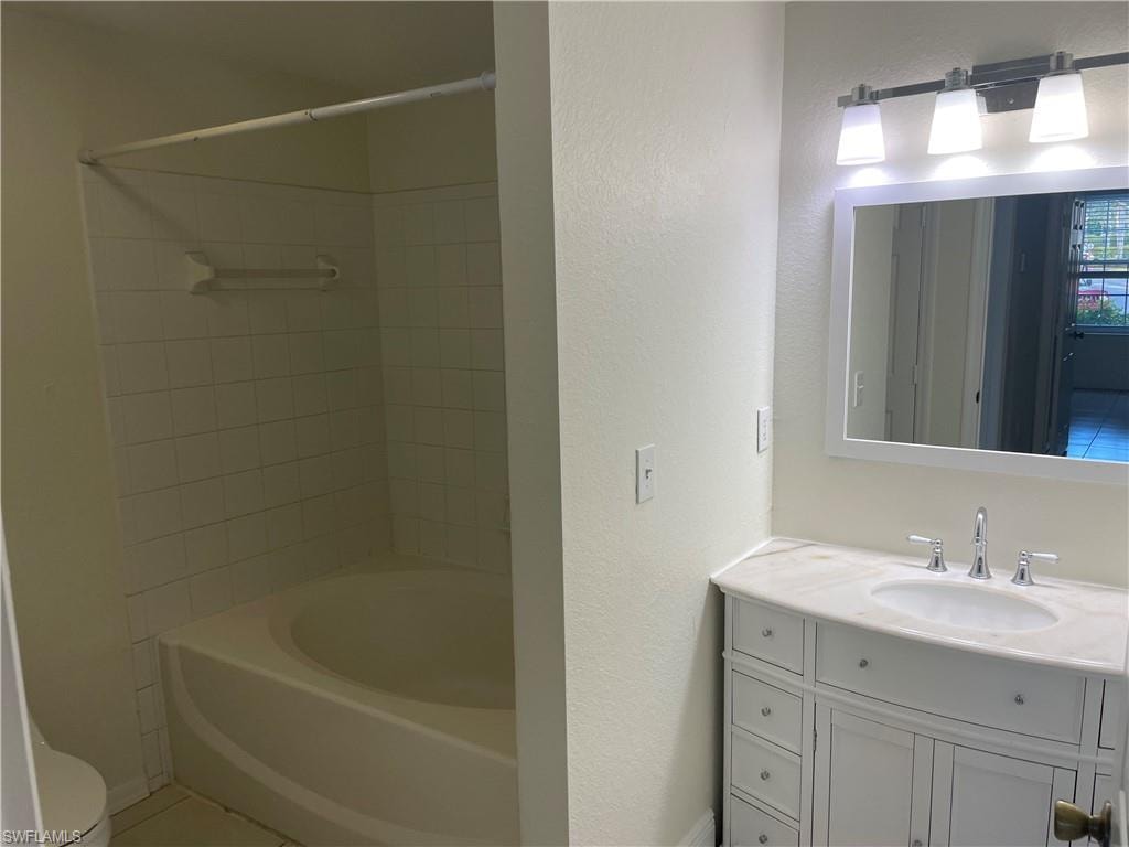 Full bathroom with vanity, washtub / shower combination, tile patterned flooring, and a textured wall