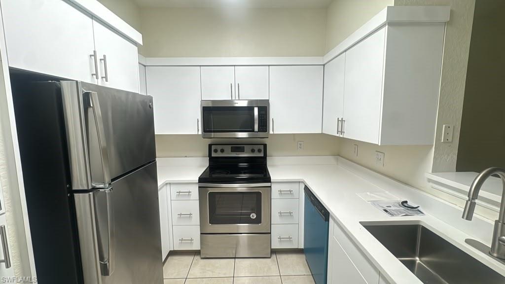 White cabinetry with brushed nickel hardware, stainless steel appliances, an undermount sink, and light-colored countertops