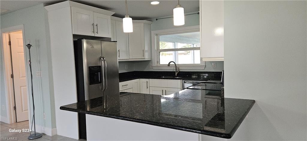 Kitchen with dark stone counters, white cabinets, decorative light fixtures, light tile patterned floors, and a peninsula