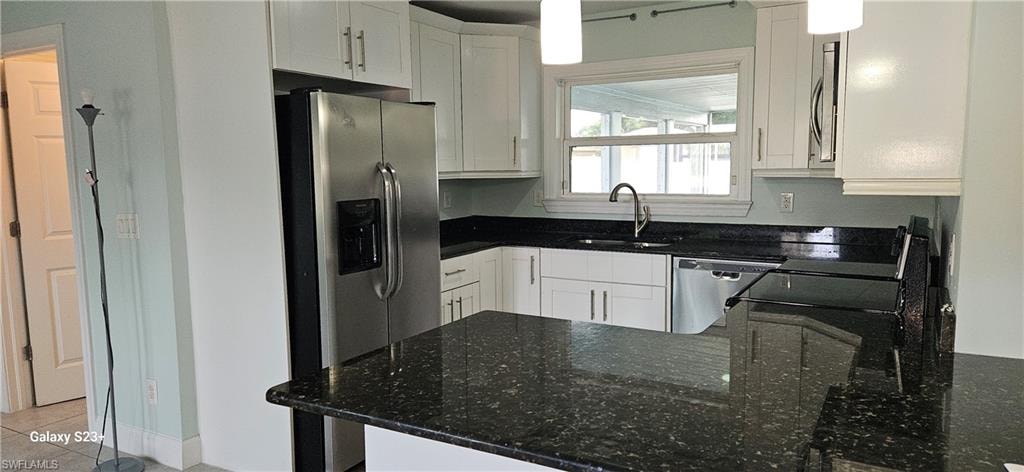 Kitchen featuring a peninsula, dark stone counters, stainless steel appliances, and white cabinets