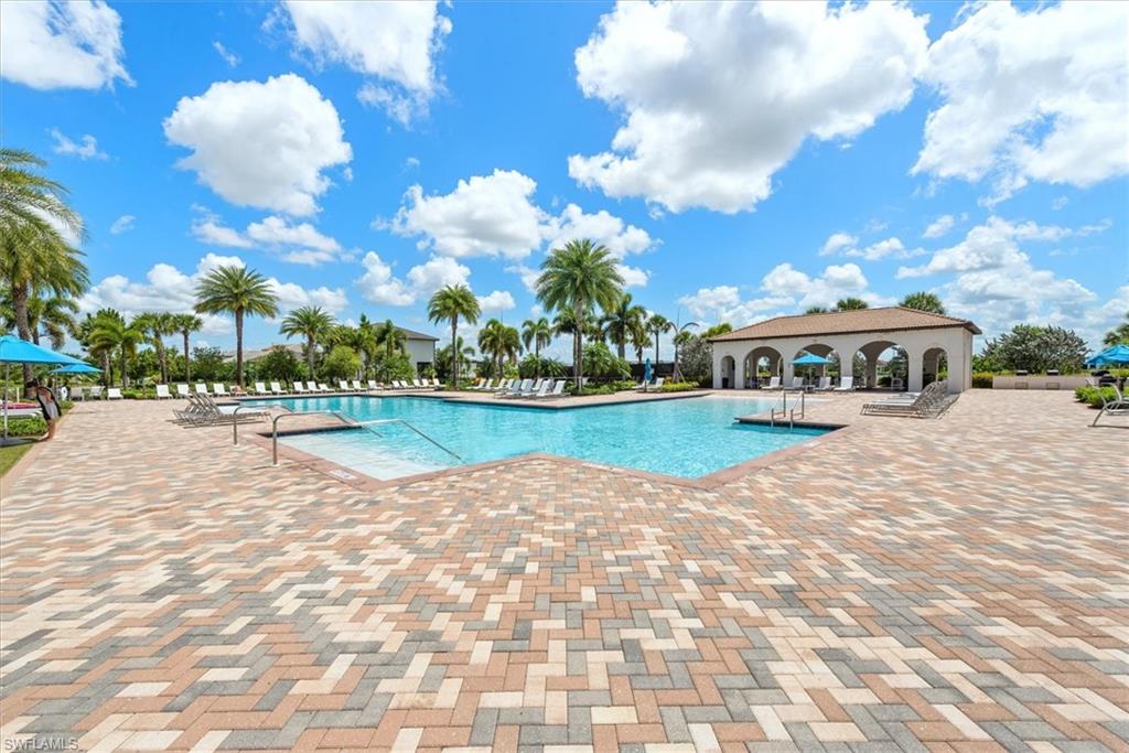 Spacious outdoor pool area featuring a large swimming pool, multi-toned paver decking, a covered cabana structure with arched openings, and numerous mature palm trees