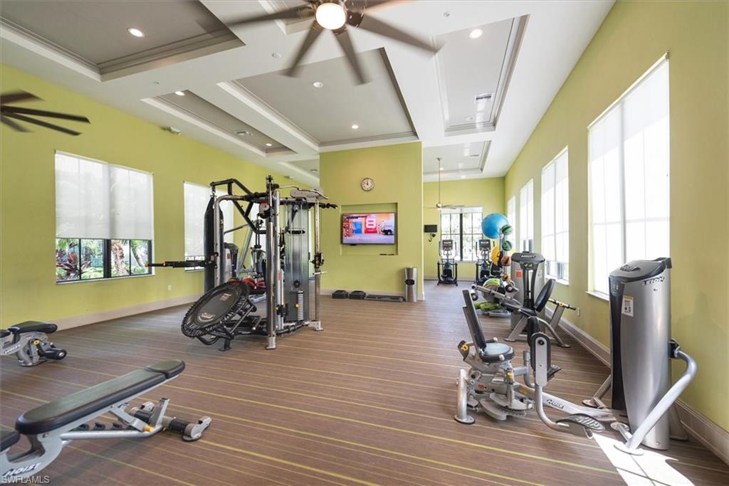Dedicated fitness room featuring multiple exercise machines, patterned wood-finish flooring, tray ceilings with integrated lighting, and multiple windows with roller shades