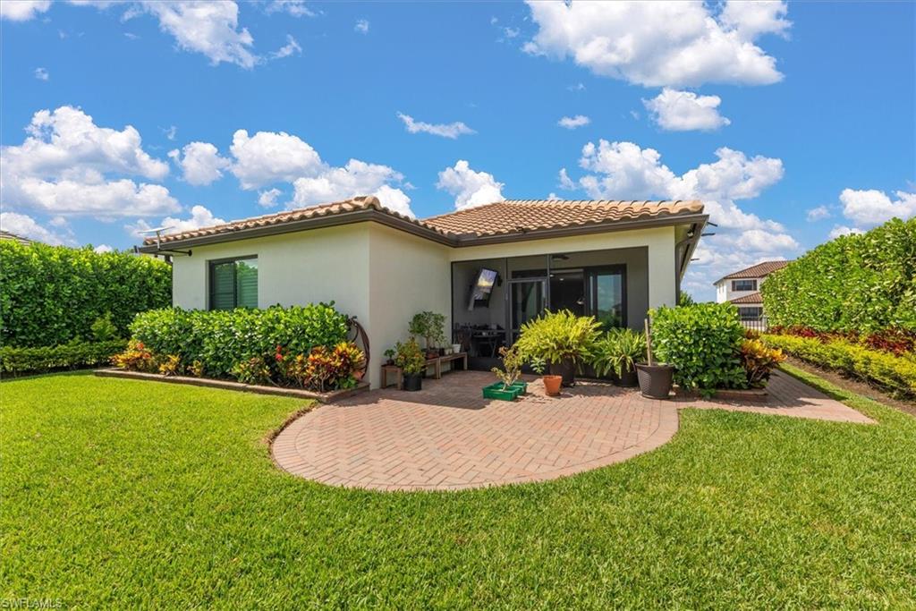 Spacious backyard featuring an extended curved brick paver patio, lush green lawn, and mature perimeter hedges