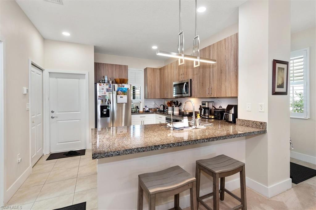 Modern kitchen featuring a breakfast bar with stone countertop, stainless steel appliances, wood-finish cabinetry, a contemporary linear pendant light fixture, and recessed lighting