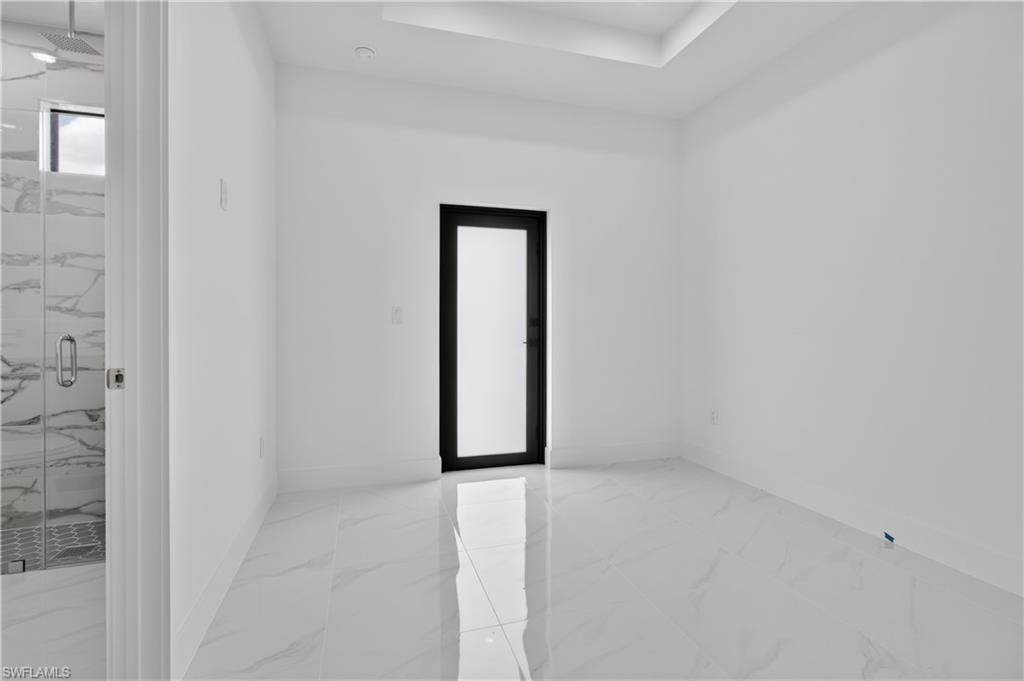 Spacious interior room featuring large format tile flooring, a black-framed opaque door, and a recessed ceiling detail
