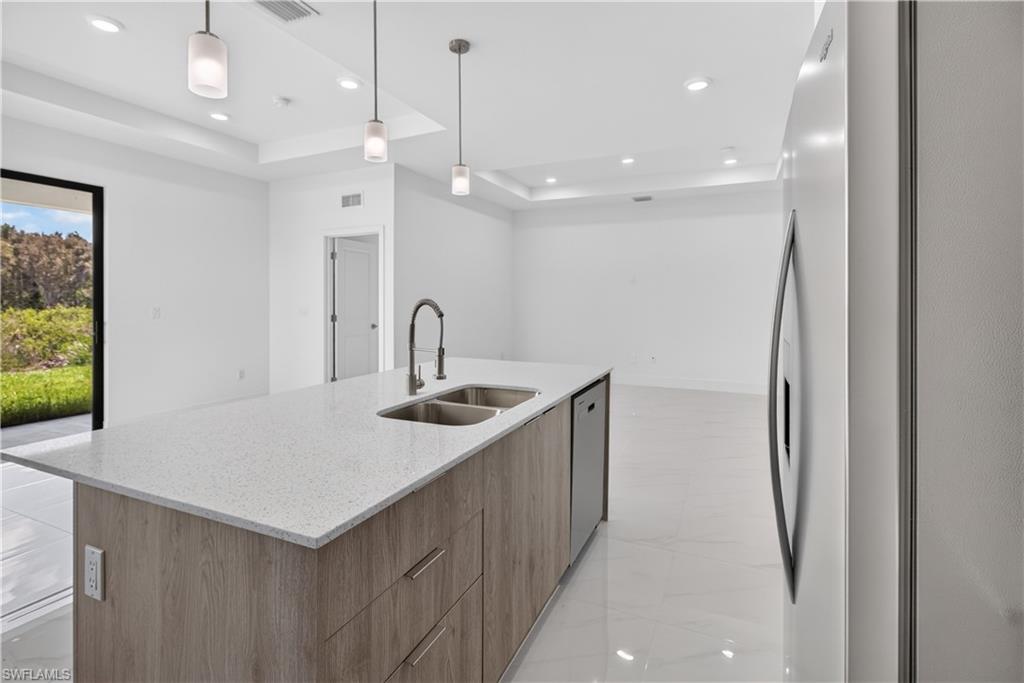 Kitchen island featuring a double-basin sink with a gooseneck faucet, light-toned wood-finish cabinetry, and a light-colored speckled countertop