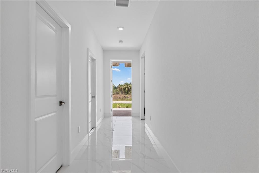 Bright hallway featuring recessed lighting, white walls, white doors with dark hardware, and glossy tile flooring