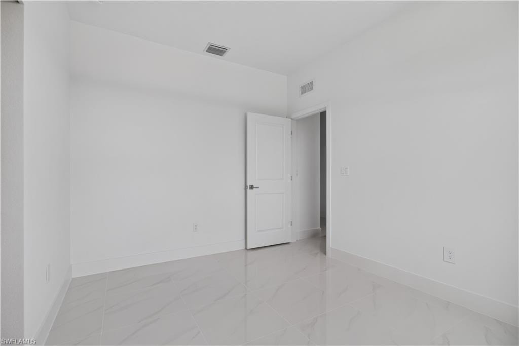 Spacious room featuring light-toned tile flooring, clean white walls, a single paneled door, and a ceiling-mounted ventilation grate
