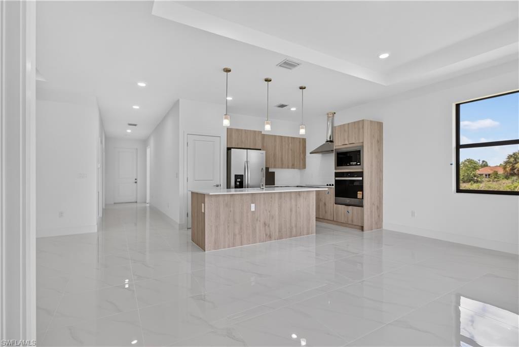 Open-concept kitchen featuring wood-finish cabinetry, a central island with countertop seating, stainless steel appliances, and contemporary pendant lighting
