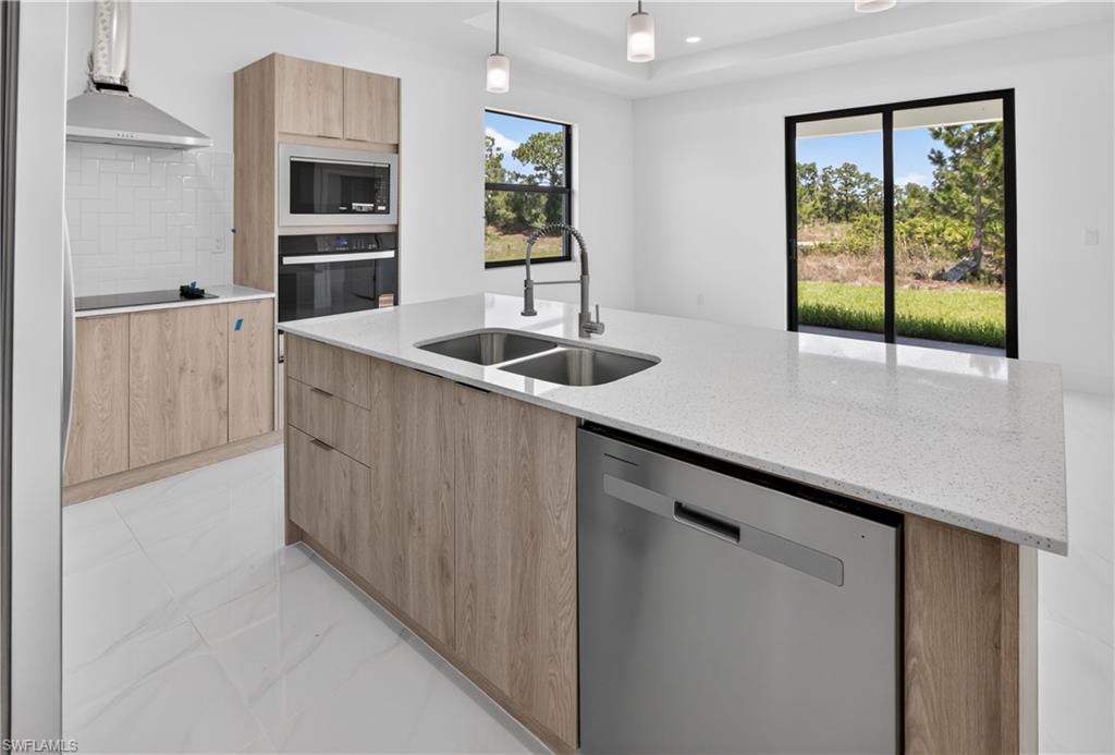 Spacious kitchen featuring a large island with an undermount double sink, stainless steel dishwasher, and light-toned solid surface countertop