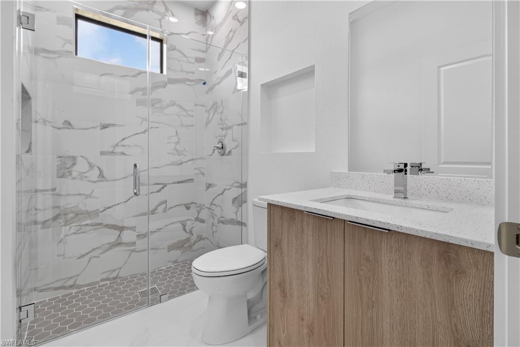 Spacious bathroom featuring a glass-enclosed shower with large format tile and hexagonal floor tile, a natural wood-finish vanity with an integrated sink and light-colored countertop, and recessed lighting