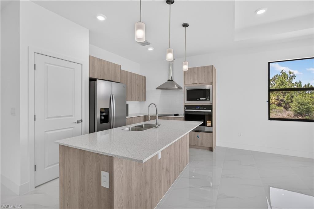 Modern kitchen featuring a large island with a light-toned countertop, stainless steel appliances, wood-finish cabinetry, and contemporary pendant lighting