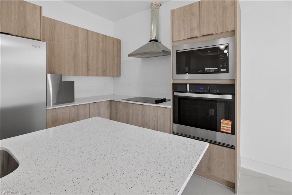 Kitchen featuring light wood-finish cabinetry, speckled white countertops, stainless steel appliances, and a built-in oven and microwave