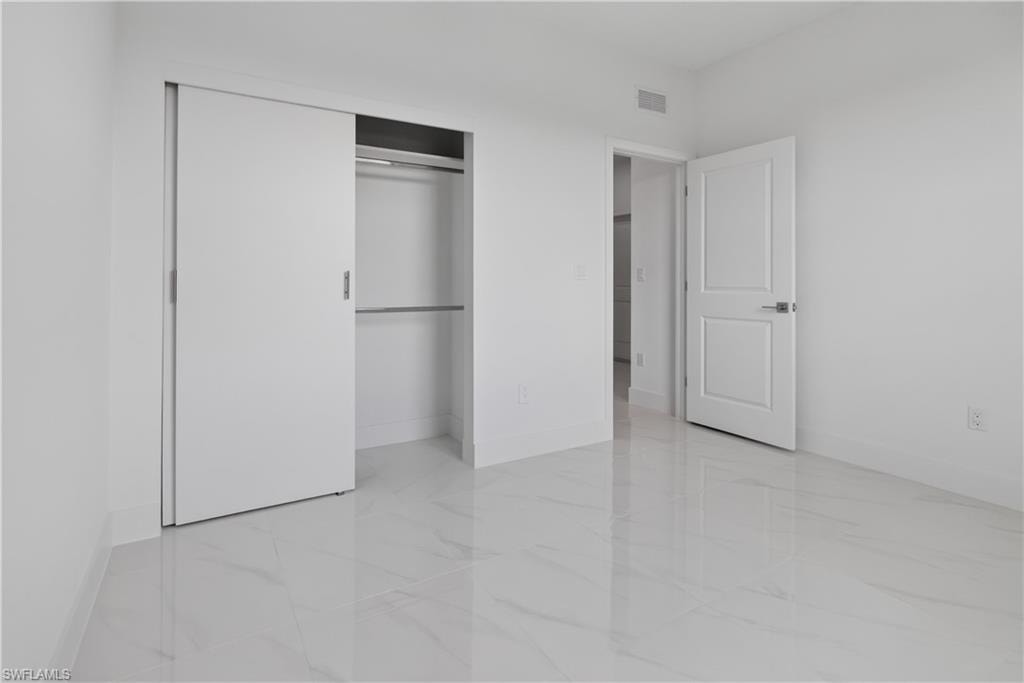 Bright interior space featuring large format tile flooring, white walls, and a sliding closet door with built-in shelving