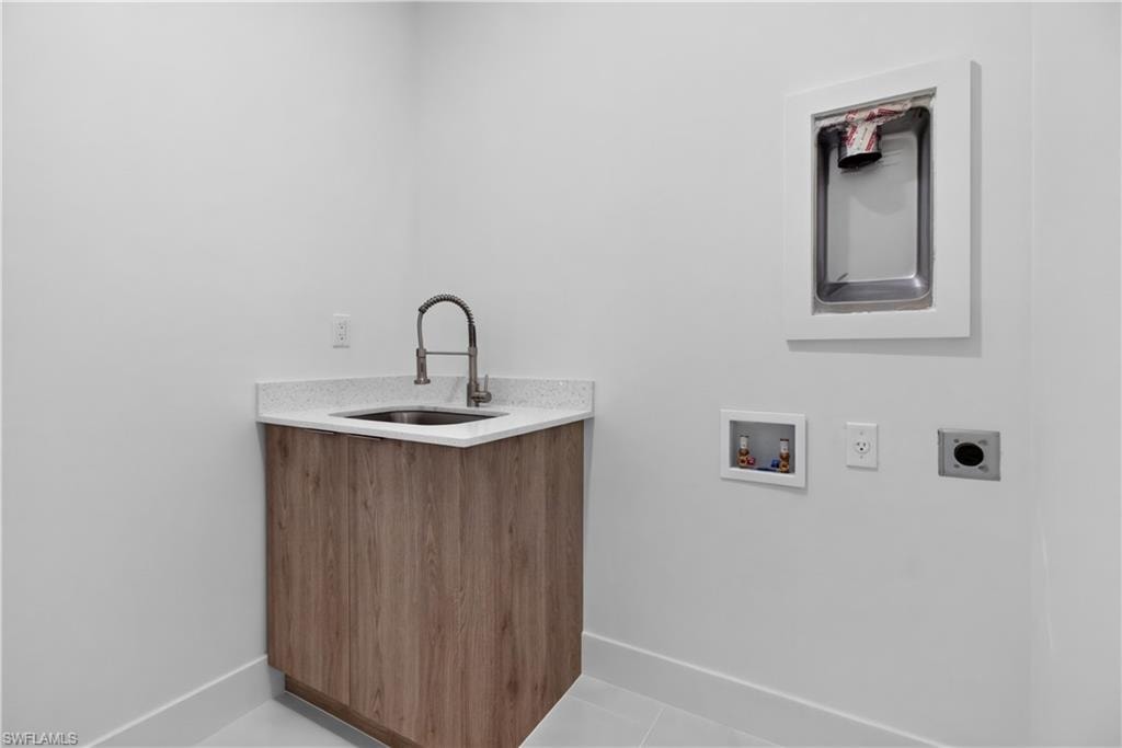Utility room featuring a wood-finish cabinet with a sink, light-toned countertop, wall-mounted laundry hookups, and floor tiling