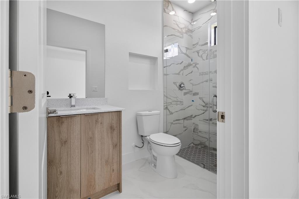 Contemporary bathroom featuring a wood-finish vanity with a speckled countertop, a mirrored wall, and a glass-enclosed shower with a marble-patterned tile surround and hexagonal floor tiles