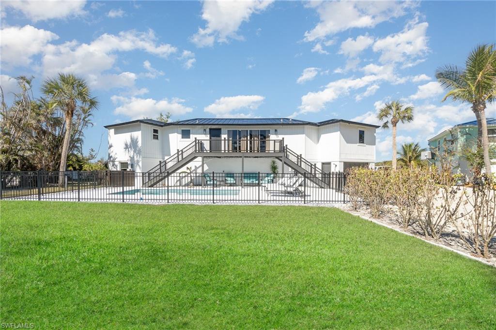 Expansive backyard featuring a manicured lawn, a fenced swimming pool, and a raised exterior deck with dual staircases