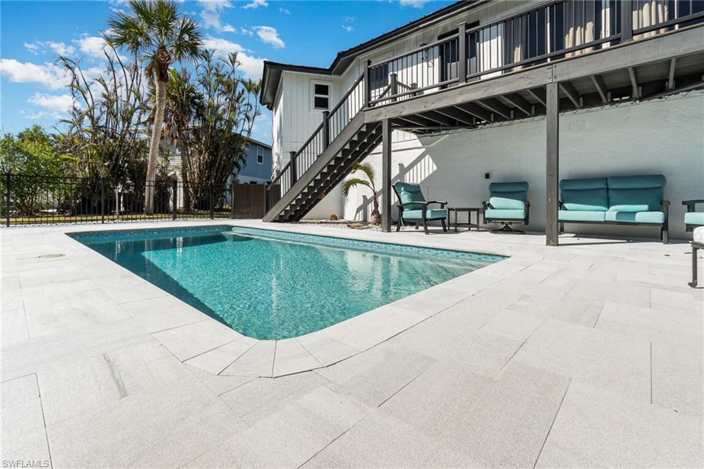 In-ground swimming pool with light blue mosaic tile, surrounded by light-colored paver decking